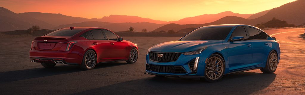 Two Cadillac V-series sedans, one red and one blue, parked in a desert landscape at sunset.