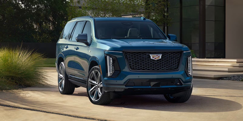 Blue Cadillac Escalade SUV parked outside a modern building with a landscaped background.